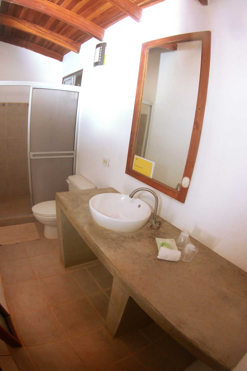 En suite bathroom at Indra Inn with concrete countertop, vessel sink, wood ceilings, large mirror, and tiled floors and shower