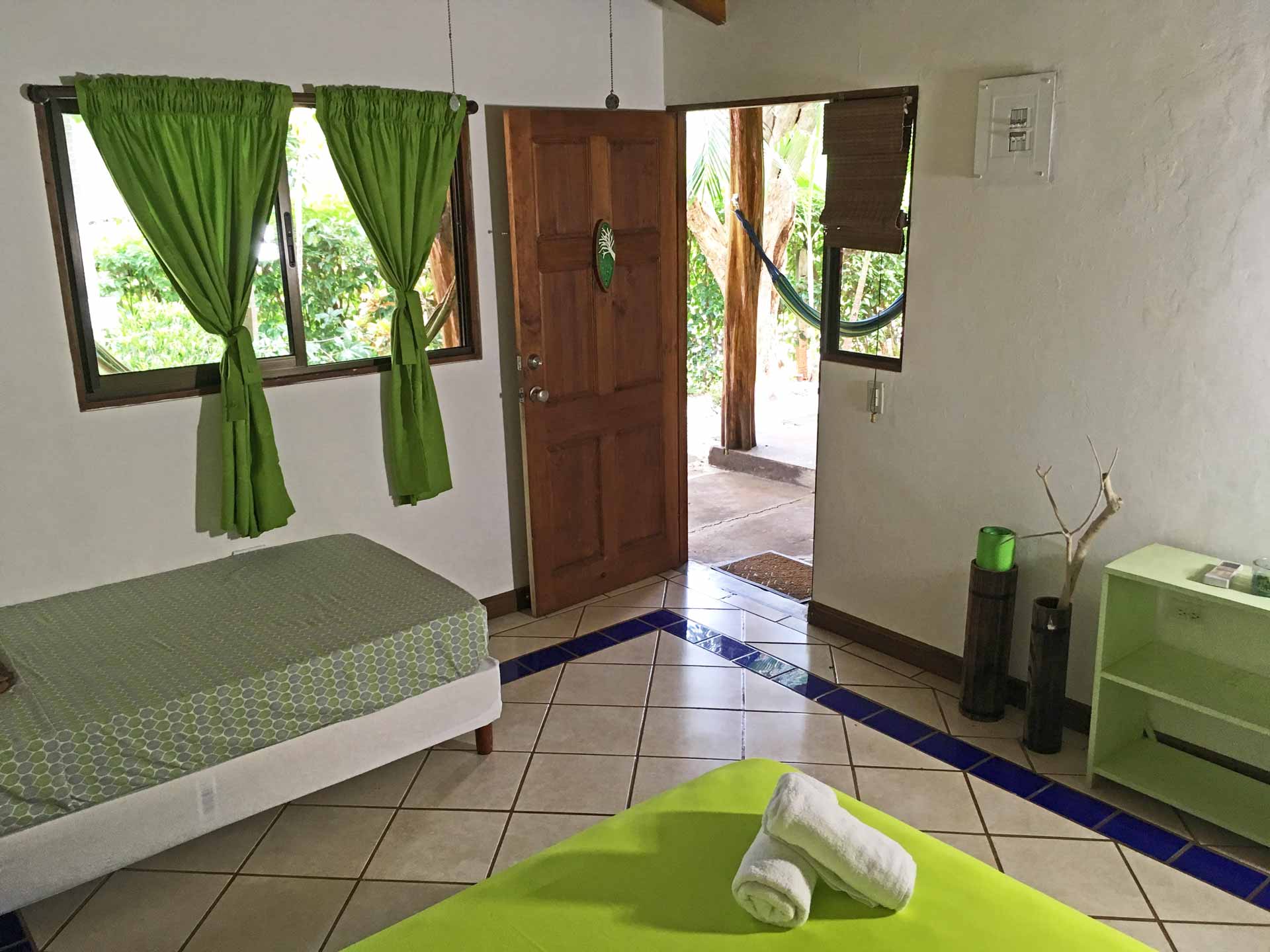 View from one bed in a triple room at Indra Inn, showing the window, door, hammock outside, yoga mat, and bookshelf
