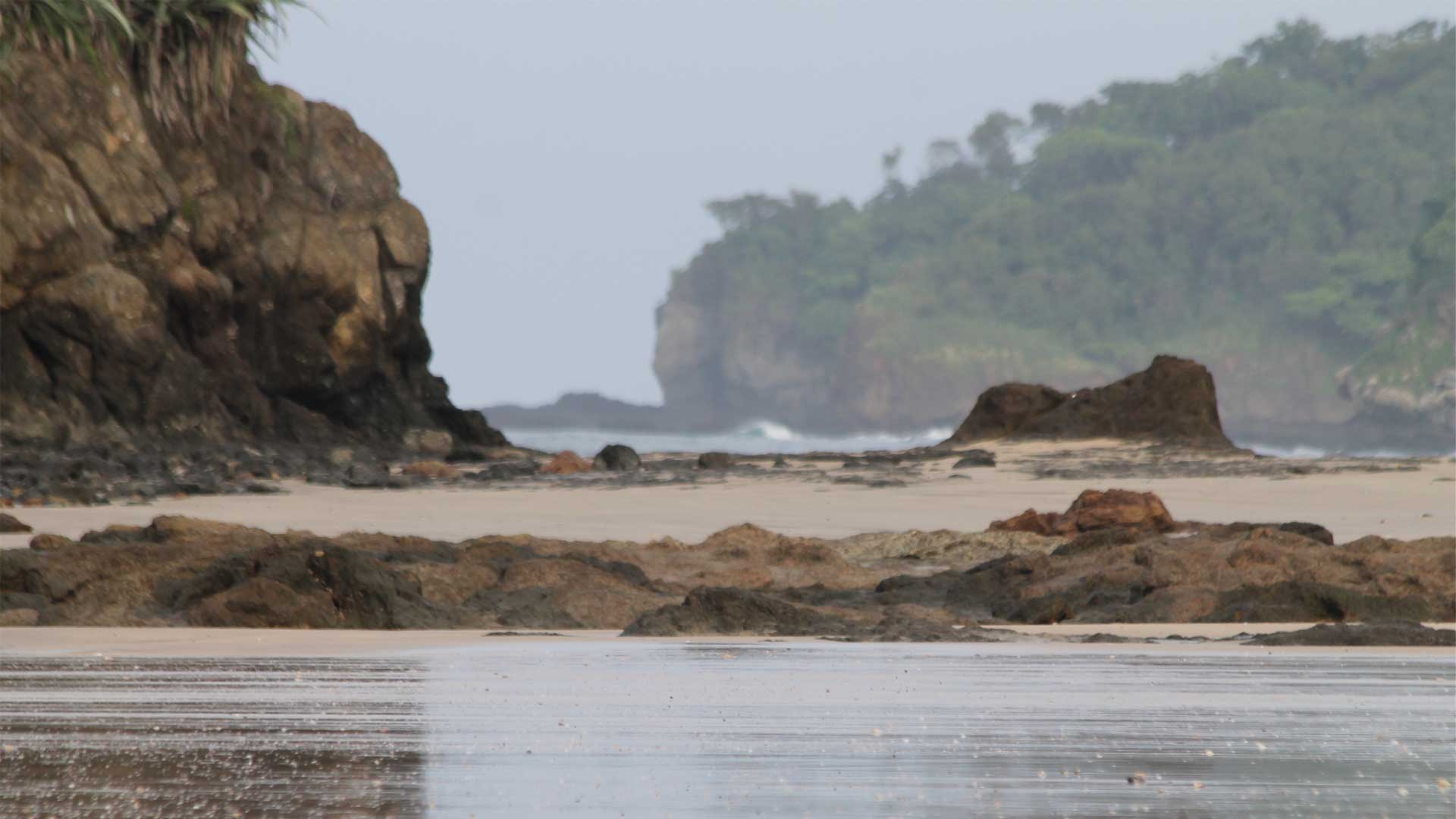 Beach rocks and boulders reflect off wet sand at low tide in Playa Grande, Costa Rica