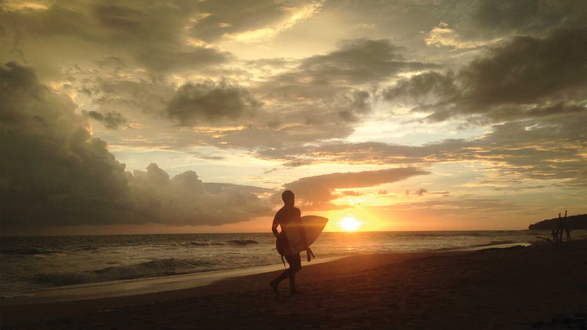 Surfer jogging with surfboard at sunset on Playa Grande beach